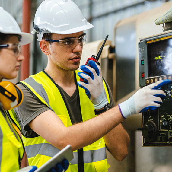 Profesionales con casco y chaleco de seguridad operando un panel de control industrial en manufactura.